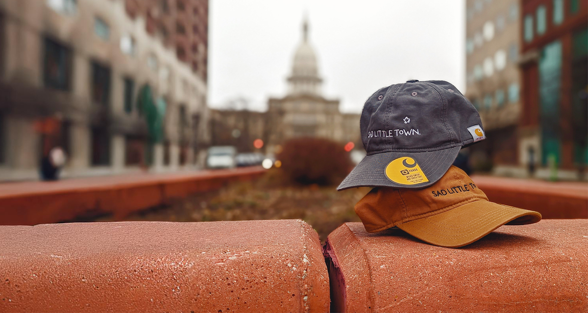 Two baseball hats with the "Sad Little Town" logo