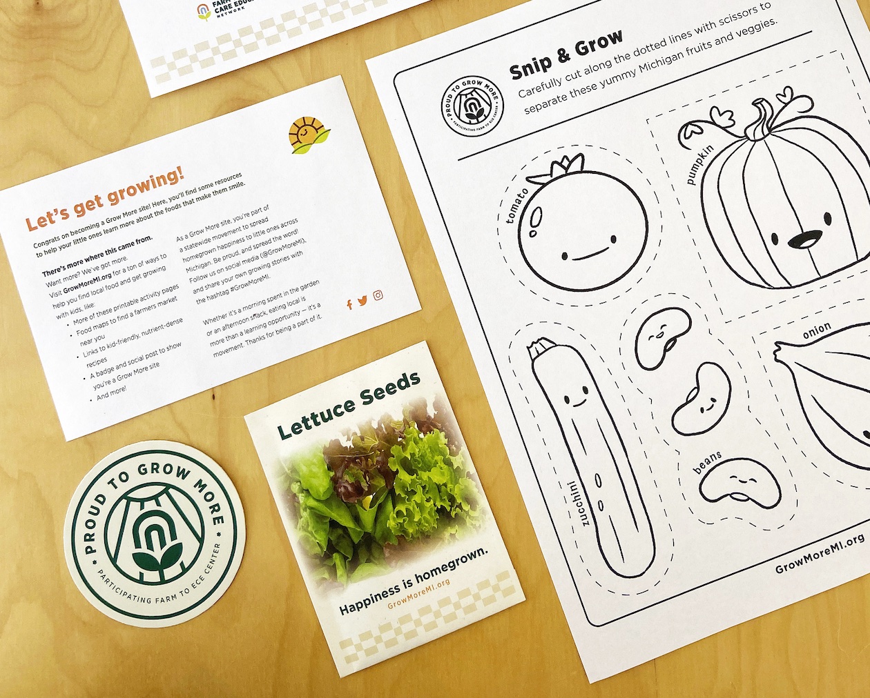 A tabletop display of activity sheets, a Grow More sticker, and a lettuce seed packer.